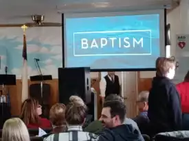 People seated in a church facing a screen displaying {{brizy_dc_image_alt imageSrc=